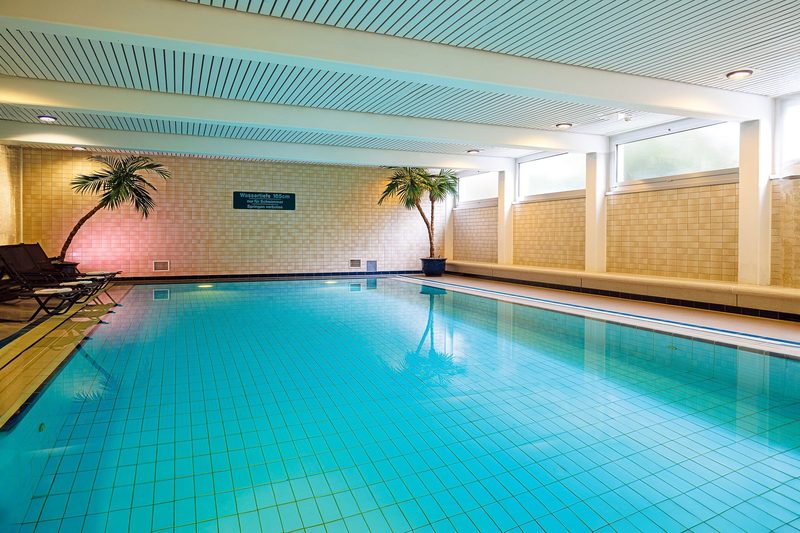 Das Hotelbecken im GenoHotel Forsbach: türkises Becken in einer hellen Halle mit Palmen
